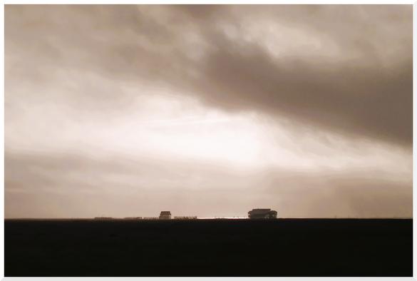 Blick über die Salzwiesen zu den Pfahlbauten von Sankt Peter-Ording. Graue Weite, wolkenvergangener Himmel, grenzenlosen Leere. Für einen kurzen Moment reißt der Himmel auf und ergießt sein Licht über die Pfahlbauten von Sankt Peter-Ording.