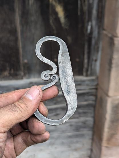 un Briquet  à silex en forme de B tenu en main en gros plan, on voit la texture de l'ancienne lime qui a servi a forger l'outil.