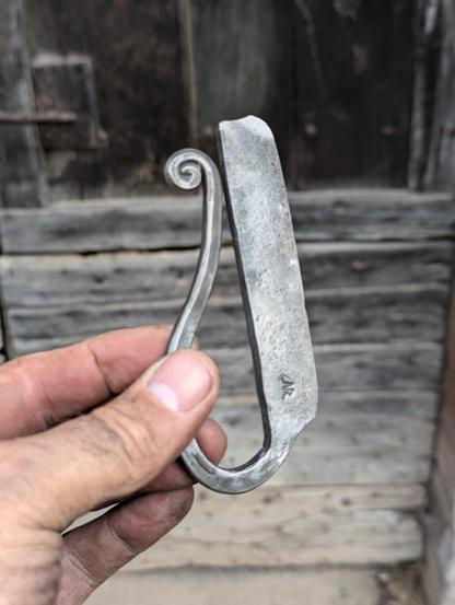 un Briquet  à silex en forme de D tenu en main en gros plan, on voit la texture de l'ancienne lime qui a servi a forger l'outil.