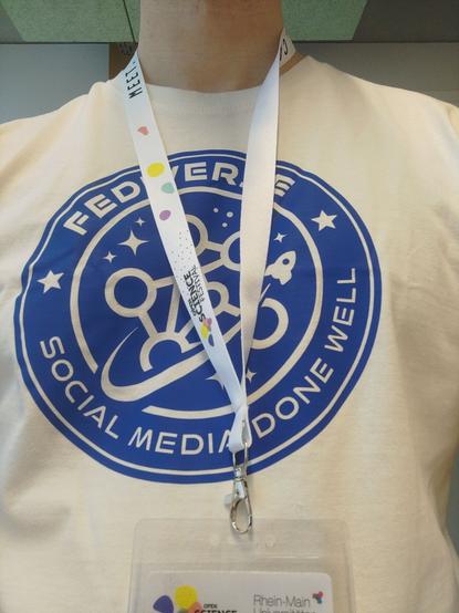 Person in a white t-shirt with the "Fediverse - Social Media done well" logo on it and a Open Science Festival lanyard around the neck