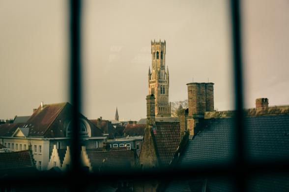 A view of the Belfort tower and the city rooftopts n the evening sun photographed through a window.