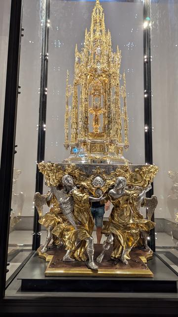 An elaborate decorative piece of religious iconography, known as a monstrance. Silver, but mainly gold, a delicate arrangement of intricate pieces, towering some eight feet tall.
