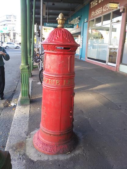 A red letter receiver with a golden decoration on top on a covered  sidewalk