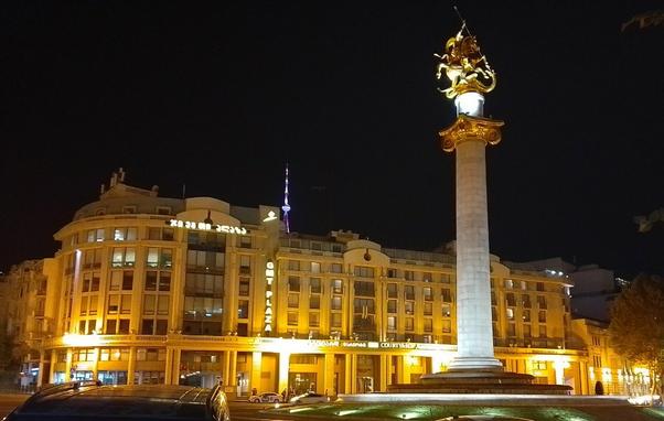 piazza indipendenza a Tbilisi, in Georgia, con un monumento in cima a una colonna, di sera