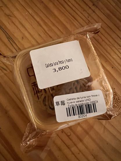 Cajita de plástico transparente con un pastelito de diseño elaborado. No se ve mucho más allá de la etiqueta gigante, que dice galleta luna fresa y huevo salado, también tiene un par de símbolos chinos. Costó 3800 colones, un poco más de $7 USD.