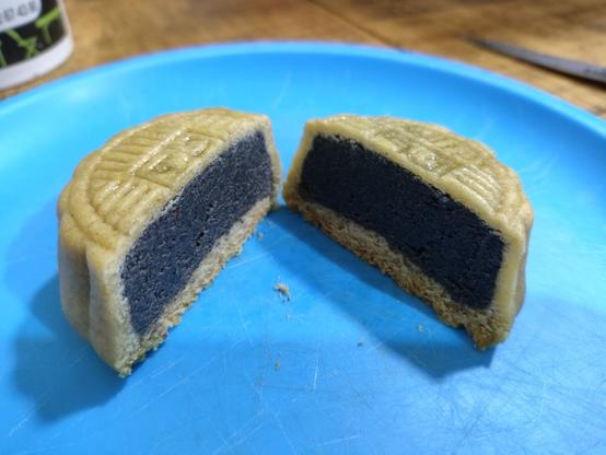 A black sesame paste mooncake cut in half showing its filling