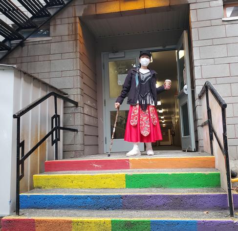 Me, standing at top of rainbow painted steps with a door open behind me.