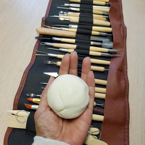 Ball of white, DIY air dry clay ball, in my left hand. Sculpting tools in roll up pouch is under my hand