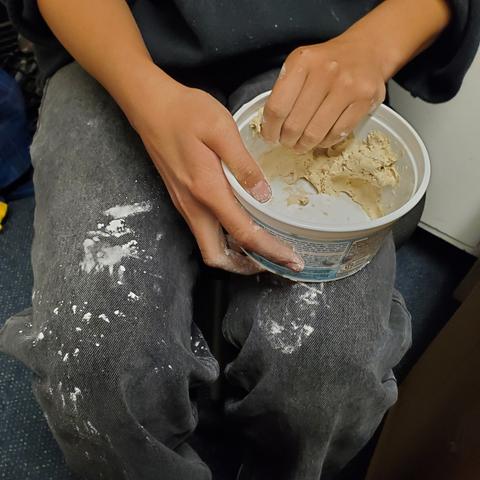 Flour on black jeans, hands holding & grabbing pre-made air dry clay from plastic container.