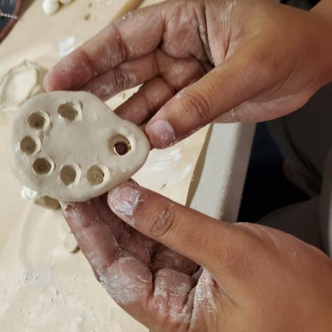 Two hands holding up miniature clay sculpted paint palette.