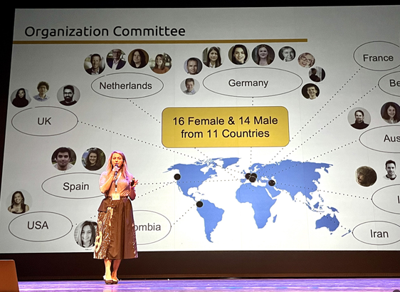 Sahar Vadathi opening Semantics 2024 conference. Sahar is standing on the big stage in fron of a slide showing the geographic distribution of the conference organising committee.