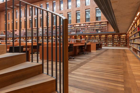 Der zentrale Lesesaal der SLUB bei Tageslicht. Im Vordergrund ist Teil einer Wendeltreppe zu erkennen, umlaufende Wandregale, Parkettboden, nicht besetzte Arbeitsplätze.