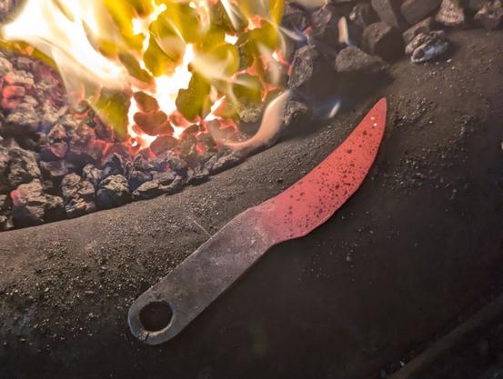 Couteau forgé encore rougeoyant à côté du feude la forge à charbon.