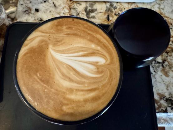 Overhead shot of a small black coffee mug filled with a yummy cappuccino sitting on a little black rubber mat.