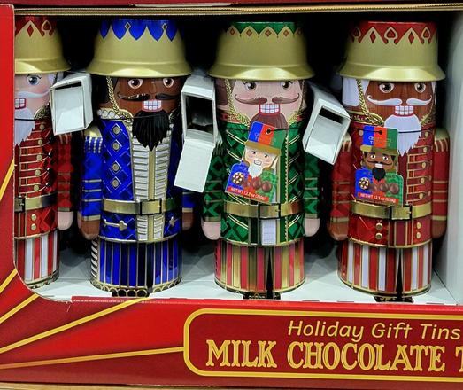 Four chocolate tins shaped as nutcrackers, each in different color: red, blue, green, brown. All placed inside a cardboard box at a warehouse store.