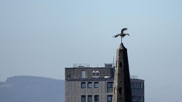 In the foreground is a tall church spire with a dragon weather-vane on the top. Beyond is a tall tower block at the university campus. And beyond that distant pale hills and trees, and a blue sky.
