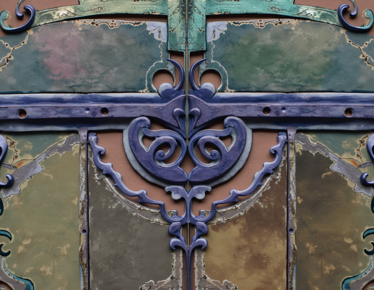 Close-up of an antique, weathered metal surface with intricate detailing, in faded purple, teal, and earth tones, rust, and patina.