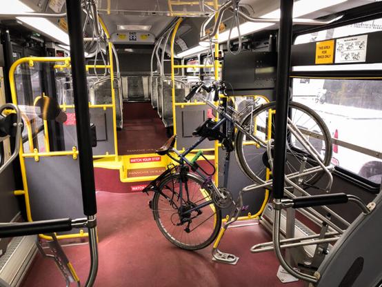 A bicycle inside a bus coach near the back doors. The front wheel is sitting in a bike rack with an arm on top of it to hold it in place.
