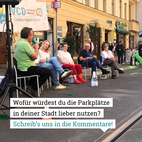 Man sieht einen Parkplatz, auf dem eine Podiumsdiskussion stattfindet. Text im Bild: Wofür würdest du die Parkplätze in deiner Stadt lieber nutzen? Schreib's uns in die Kommentare!