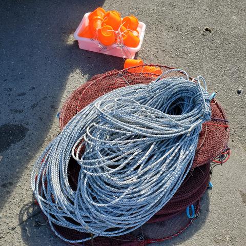 Round netted crab traps, lots of blue/white rope & bright orange bait containers. On the cement ground.
