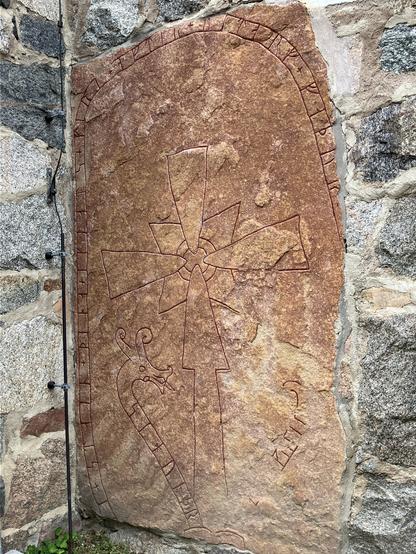 Red sandstone block with runes carved on it. It is surrounded by grey stones, having been incorporated into the wall of the church at Gamla Uppsala.