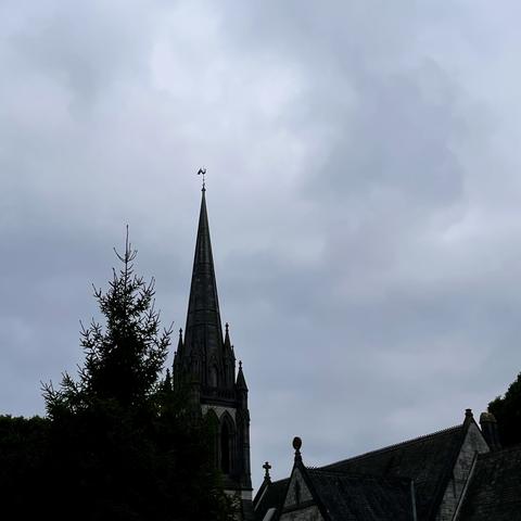 A dark church spire is visible against a cloudy sky, partially obscured by a tree. The architecture features Gothic elements.