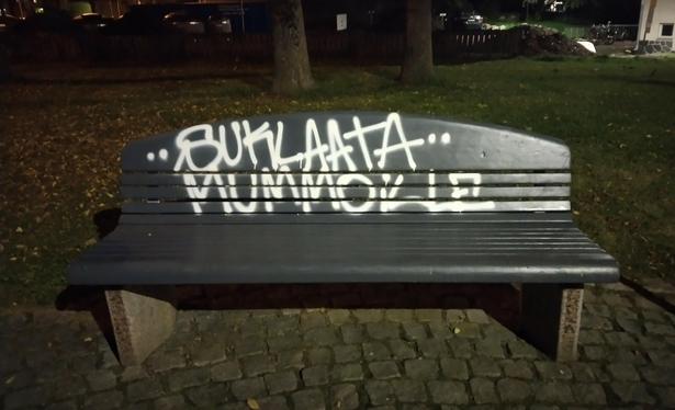 Puistonpenkki, johon on valkoisella sprayllä tägätty koko selkänojan kokoinen teksti suklaata mummoille.