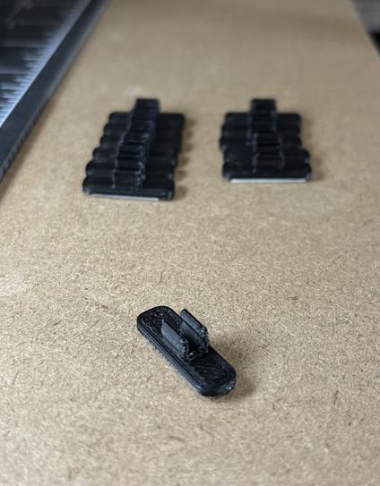 A usb cable clip printed in black filament with 11 more clips behind in two columns. 

The clip is a rectangular shape with rounded ends, with a curve shape on top to hold a USB cable.