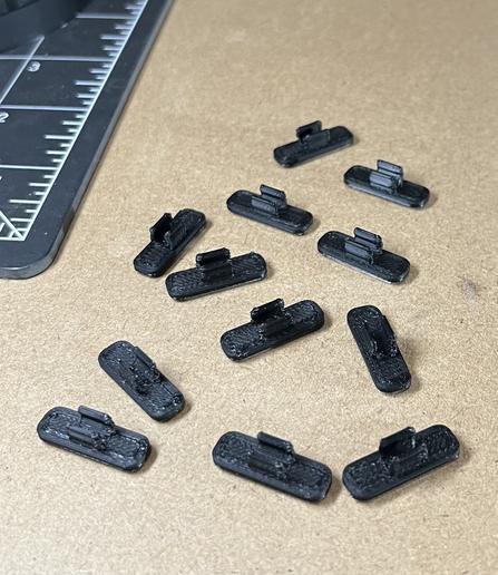 12 USB cable clips printed in black filament spread out on a work surface.
