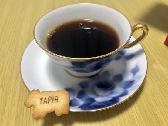 ホットコーヒーに、たべっこどうぶつビスケットが添えられた写真。ビスケットに「TAPIR」と書いてある。