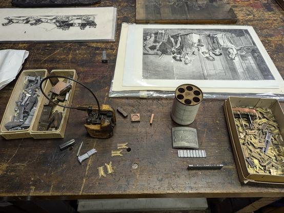 Scarred and scratched wooden table top. A freshly printed print, a scattering of type in a box. A wooden type form mould.