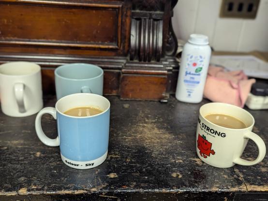 Multiple cups of tea with milk on a wooden scarred and scratched shelf. Bottle of talcum powder in the background