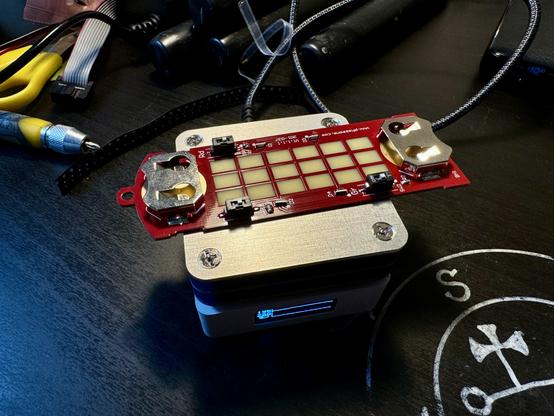 The badge with all the components populated cooling on a tiny USB-C powered hot plate with an OLED screen. Next to a sigil of Marbas of course.