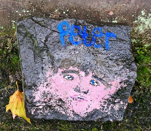 A face painted, which is blurred around the edges, painted on a rock with the name Peter above it.