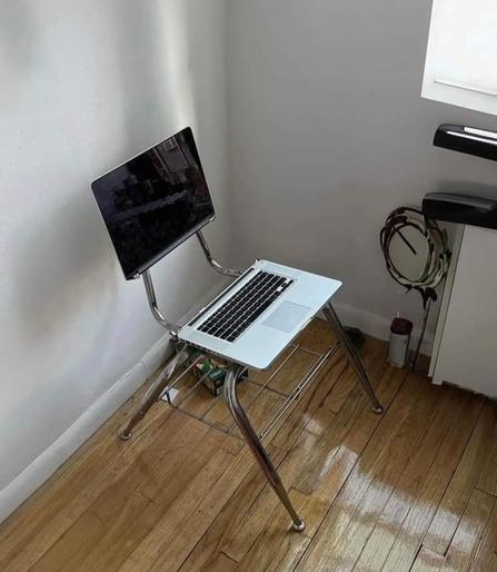 Photo of a metal school chair made with laptop parts so the bottom half is the seat, while the back part is the display.