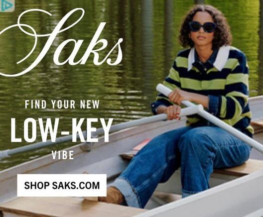 A screenshot of an advertisement for Saks. The text says, “FIND YOUR NEW LOW-KEY VIBE. SHOP SAKS.COM.” The ad shows a young female model sitting in a rowboat on a pond. She is wearing large dark sunglasses, a rugby-style shirt with a wide white collar, and alternating wide stripes and that are light green and dark blue. She is also wearing slightly baggy medium-dark blue jeans that are rolled up at the cuffs.