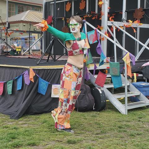 Clown Car Drag performer doing solo performance on grass, beside stage, pointing out at crowd.