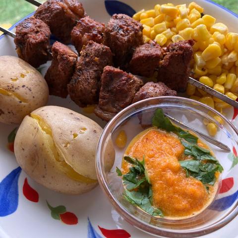 Skewers of beef, boiled potatoes, corn, and a  pepper sauce topped with cilantro