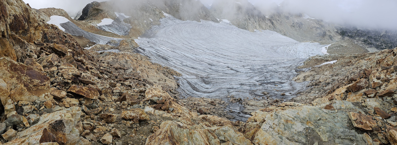 A striated glacier is shown within a bowl created by alpine peaks