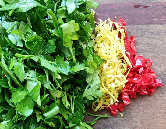 viel Petersilienblätter, Zitronenzesten + gehackte rote Chili auf einem Brett