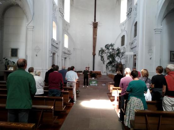 Ein Kirchraum mit Menschen in den Bänken und einem Mensch vor dem Altar.