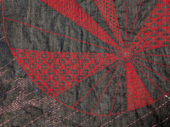 Blue denim fabric stitched with a LOT of sashiko in red - five different patterns radiating from a point off centre to the right, with some purple at bottom left