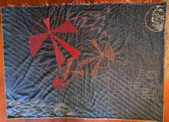 Big denim sashiko quilt cover. It is an abstracted design with four intersecting circles (reds and oranges) of diminishing (or increasing...) sizes in the centre which have segments full of different sashiko stitchwork, abstract purple whispy cloud forms above and right of these, a 3/4 white moon at top right, abstract pale grey-blue mist forms bottom right, White sashiko wave forms at bottom left ... and behind all are vertical and diagonal lines of pale blue and deep blue