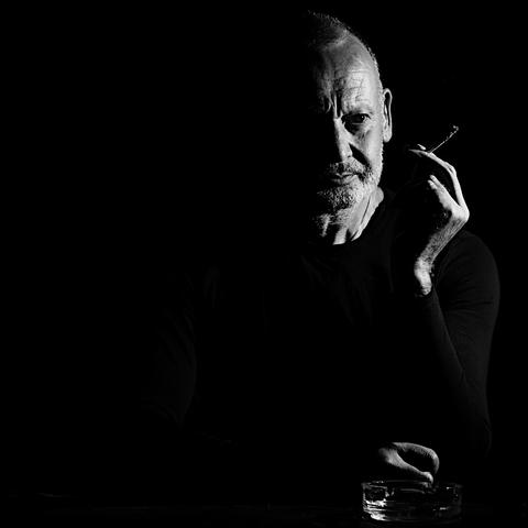 Portrait of a mature man smoking a cigarette, dramatic lighting in the low key chiaroscuro style.