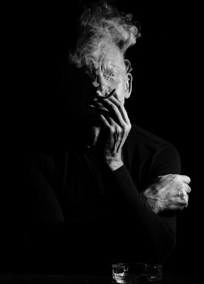 Portrait of a mature man smoking a cigarette, face obscured by the smoke. Dramatic lighting in the low key chiaroscuro style.
