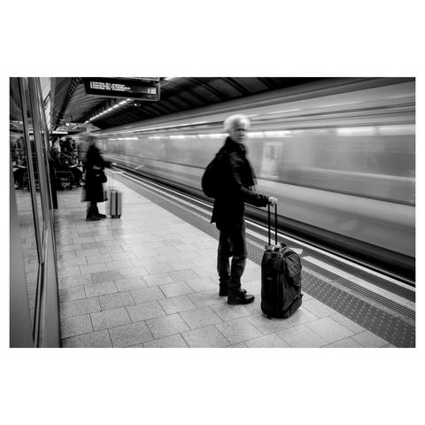 Black and white photo of passengers standing on a tube platform in front of a speeding train.