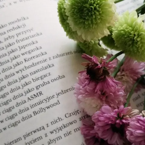 Zdjęcie otwartej książki z jesiennymi kwiatami. Widać fragment tekstu, ale bez kontekstu nie ma on sensu, więc pełni jedynie funkcję estetyczną