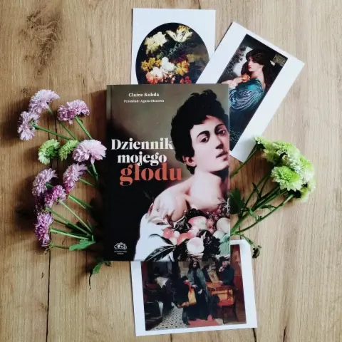 Zdjęcie typu flat lay (czyli ułożone przedmioty na powierzchni i sfotografowane z góry). Widać na nim papierowy egzemplarz książki "Dziennik mojego głodu", pocztówki z obrazami z Tate i jesienne kwiaty.