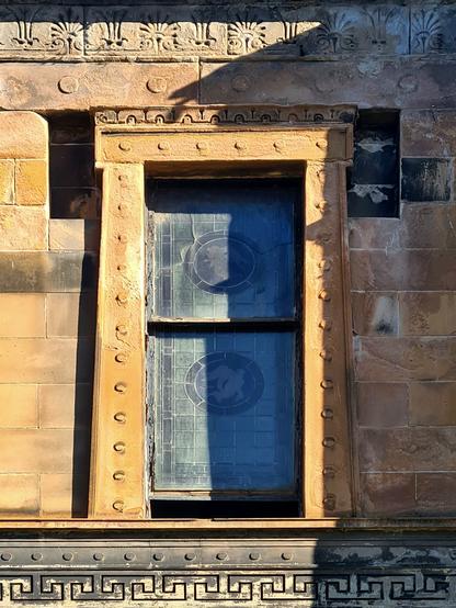 A window in a blonde sandstone building with a Classical style surround and decorations.