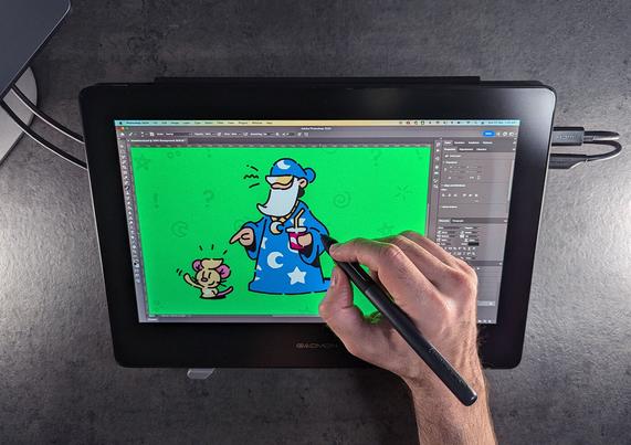 A person using a stylus on a graphic tablet to draw a cartoon character in a blue robe with stars, holding a soda, next to a small creature, on a green background.